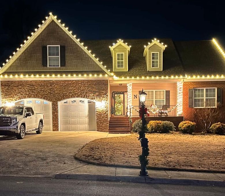 A home lit by LitXperience at night, with warm white lights tracing every roofline, dormer and porch column